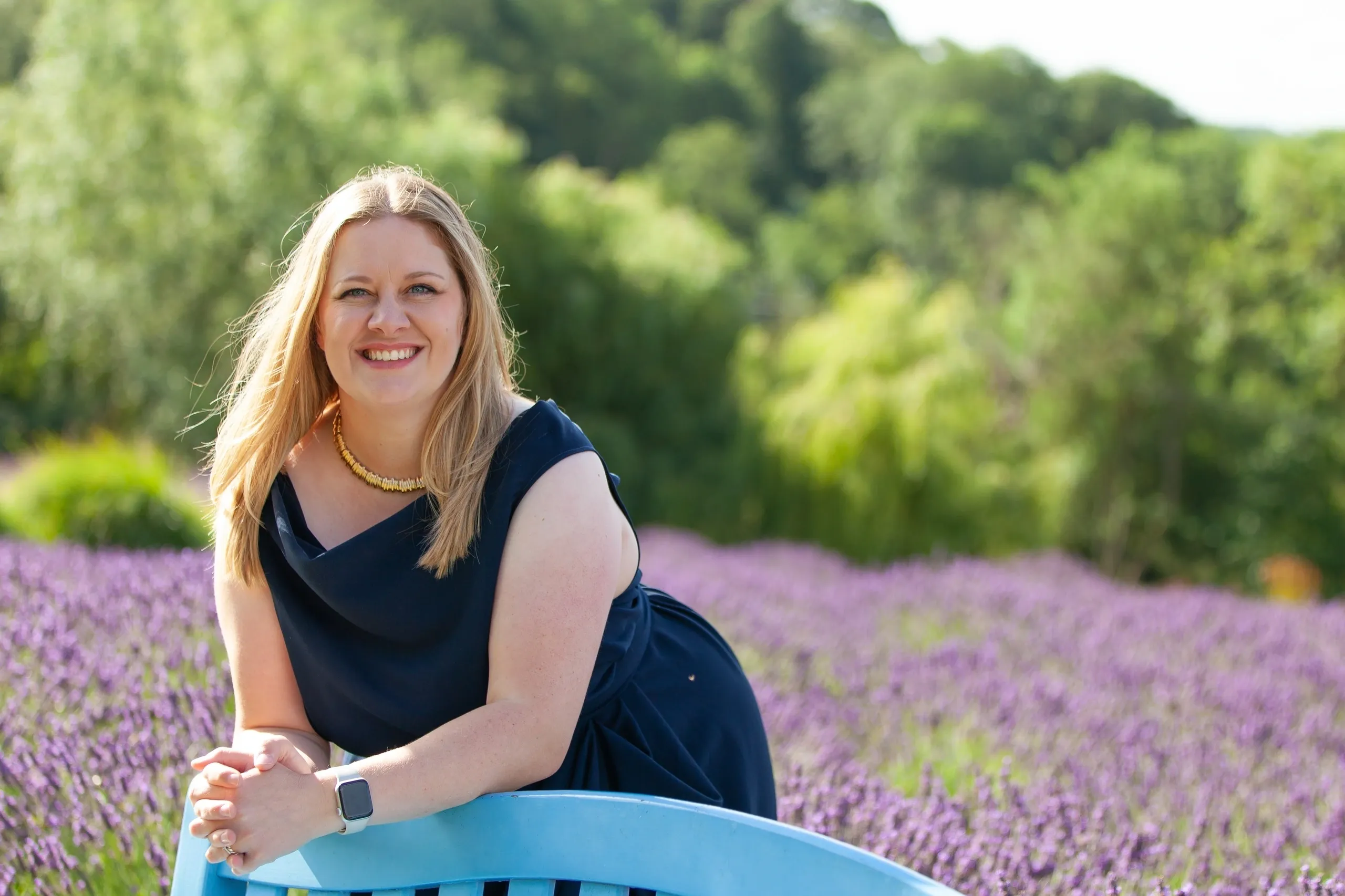 Emily Harding wearing a navy dress leaning on a blue chair in a lavender field.