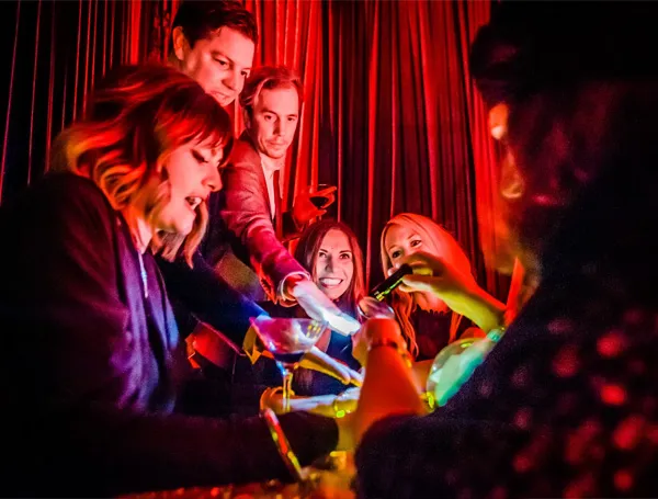 Group of friends enjoying a reading together under warm, red lighting in a lively social setting.
