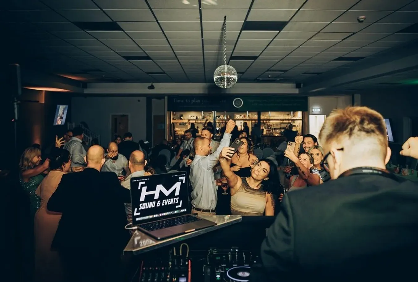 Harry performing at a party with a crowd dancing and taking selfies under a disco ball.