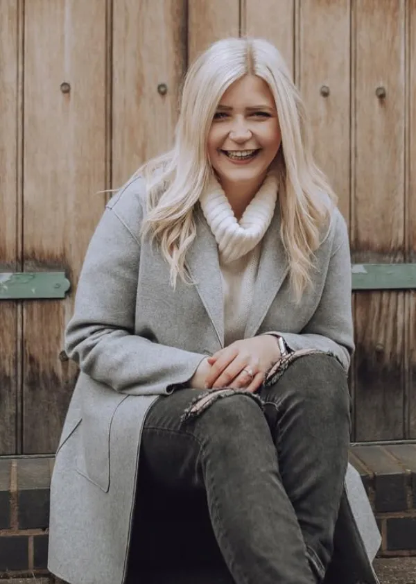 Jessica wearing gray coat and cream sweater sitting in front of wooden door.
