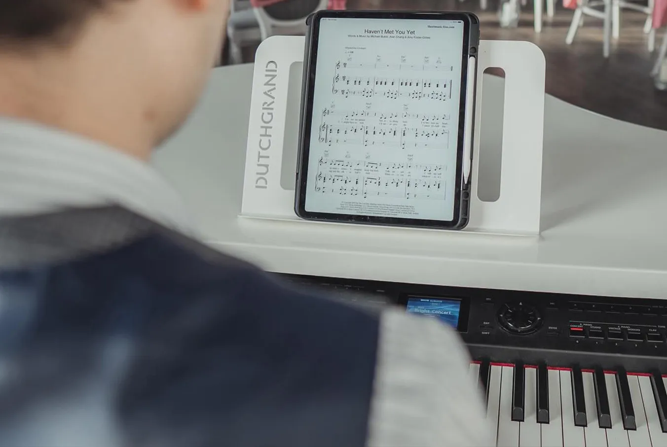 Man playing keyboard piano with digital sheet music displayed on tablet in a Dutch Grand music stand.