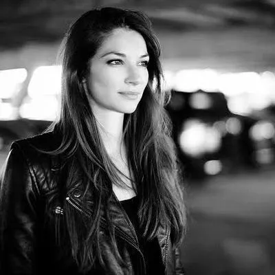 Young woman with long hair wearing a leather jacket looking off to the side in black and white.