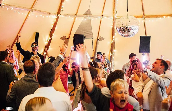 Energetic crowd dancing and celebrating indoors with festive lights and a disco ball overhead.