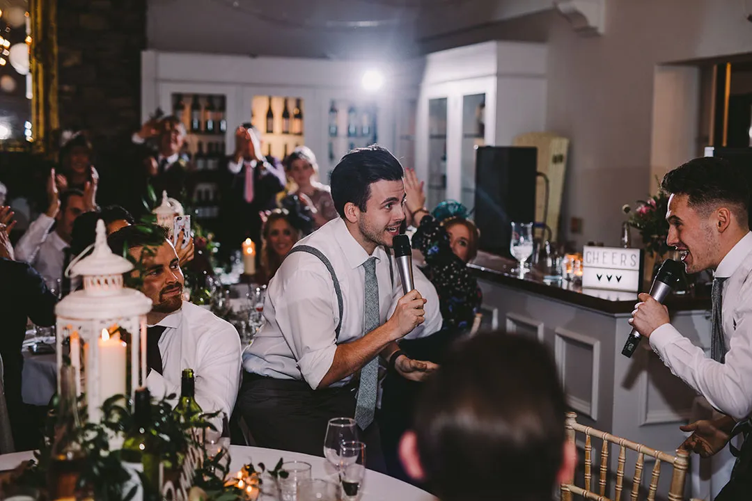 Two men in white shirts and ties singing into microphones at a festive dinner event.