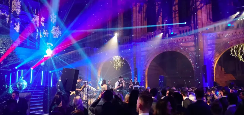 Live band performing on stage with colorful lights and crowd dancing at a vibrant night event.
