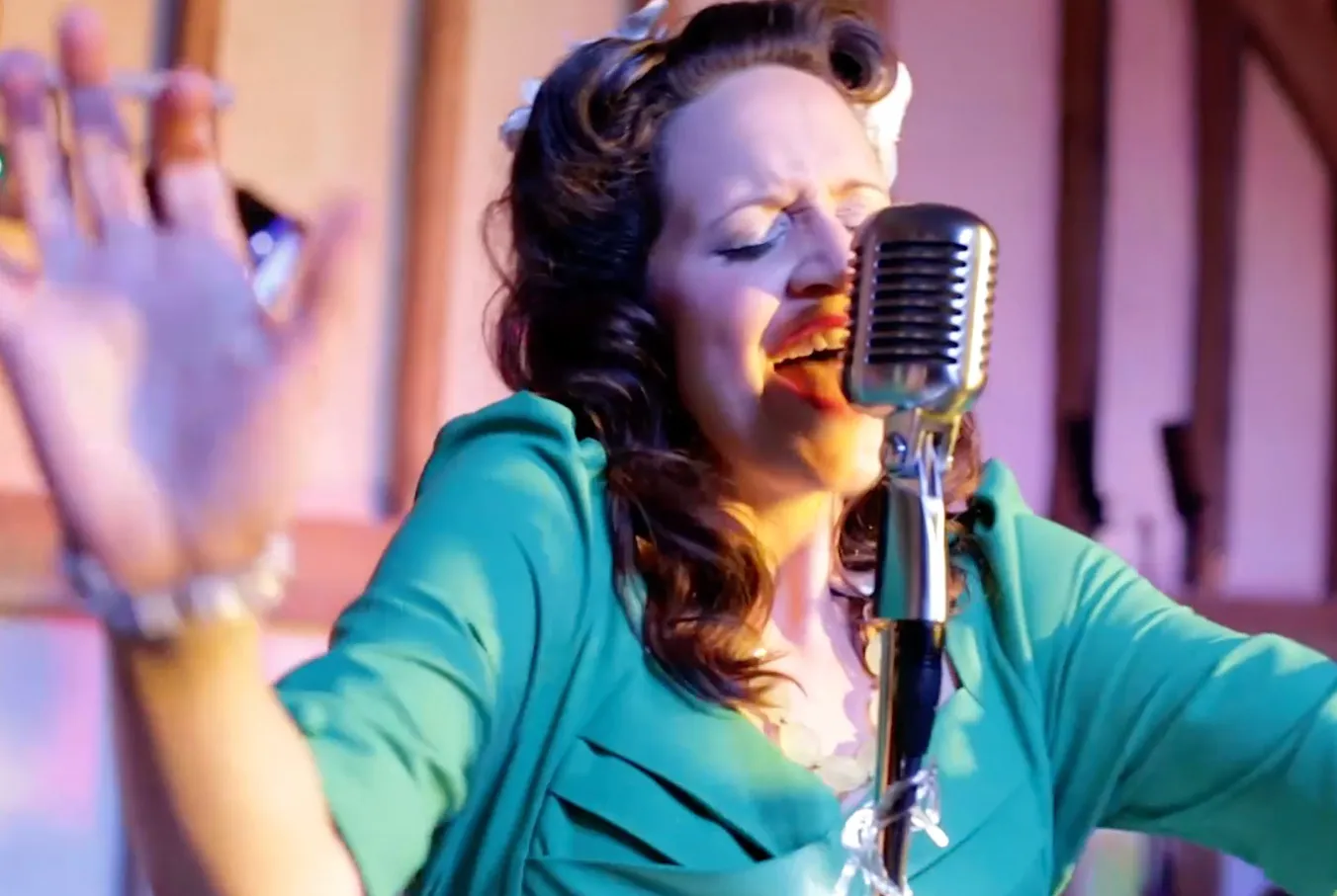 Woman in teal dress passionately singing into vintage microphone with hands raised.