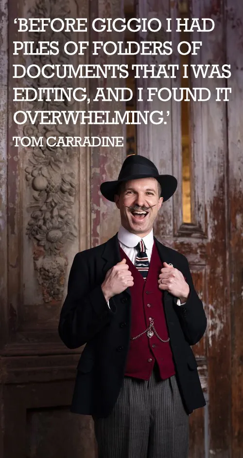 Man in vintage suit and hat smiling, standing in front of ornate wooden door with quote about Giggio.