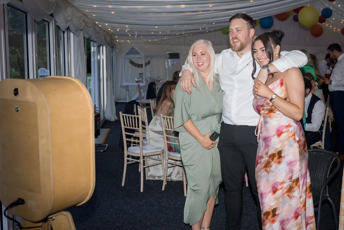 Three people smiling and posing for a photo in a decorated tent at a social event.