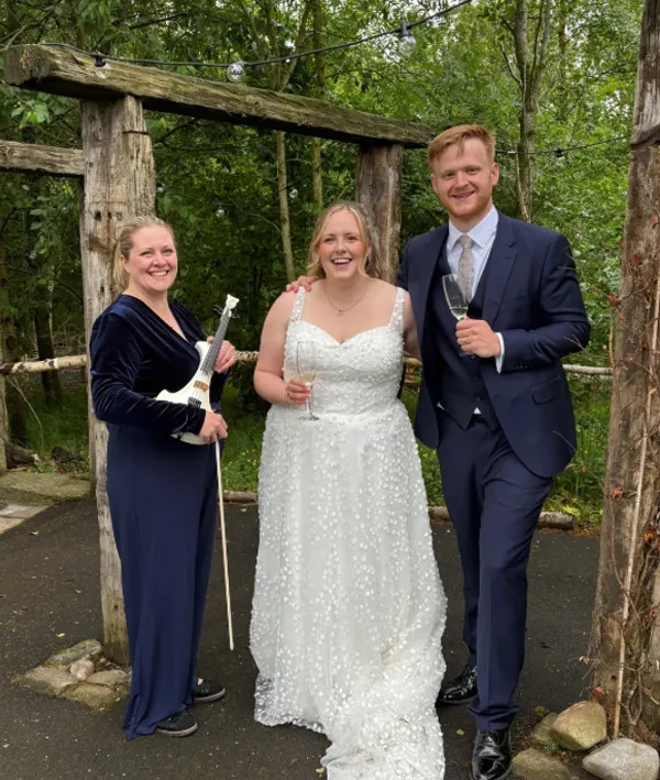 Bride in white dress and groom in blue suit Emily holding a small white violin outdoors.