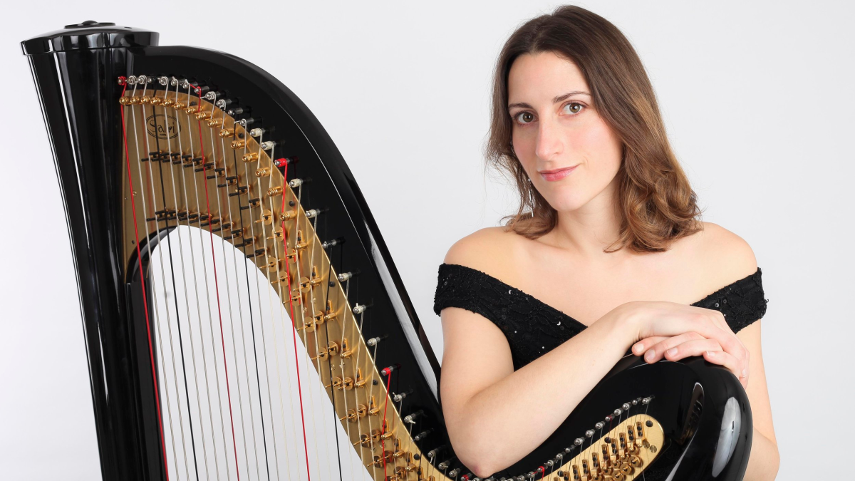Cecily Beer in black dress posing with her black harp against a white background.